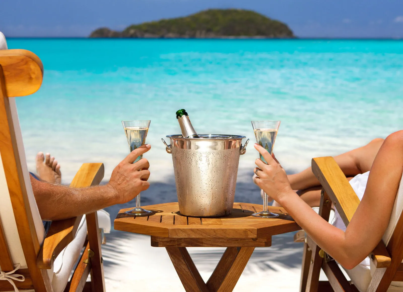 Couple sitting on deckchairs on a beach drinking wine - Cadillac Travel