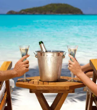 Couple sitting on deckchairs on a beach drinking wine - Cadillac Travel