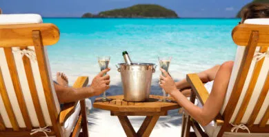 Couple sitting on deckchairs on a beach drinking wine - Cadillac Travel