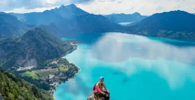 Woman sat at the top of mountain with blue lake in the background - Cadillac Travel