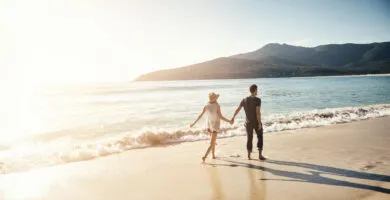 Couple holding hands and walking on beach - Cadillac Travel