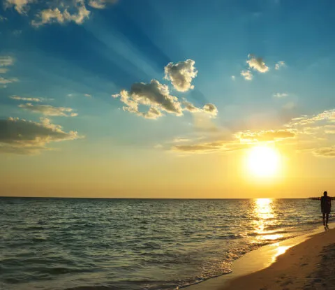 Man walking on beach as the sun sets - Cadillac Travel