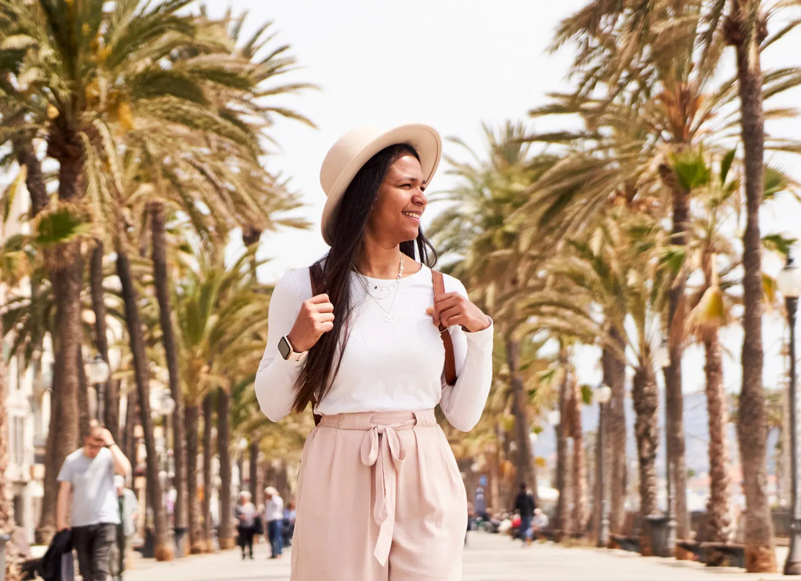 Woman walking down a street with lots of palm trees - Cadillac Travel