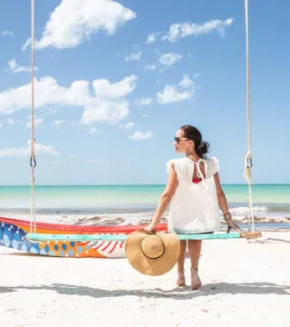 Woman sitting on swing on a tropical beach - Cadillac Travel