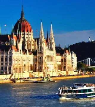 River cruise in the day with historic building in the background - Cadillac Travel, Detroit, MI
