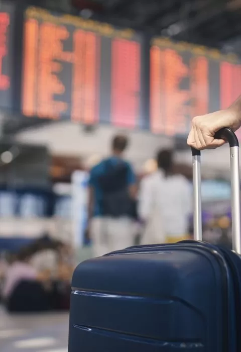 Hand of man while holding suitcase against arrival and departure board at airport